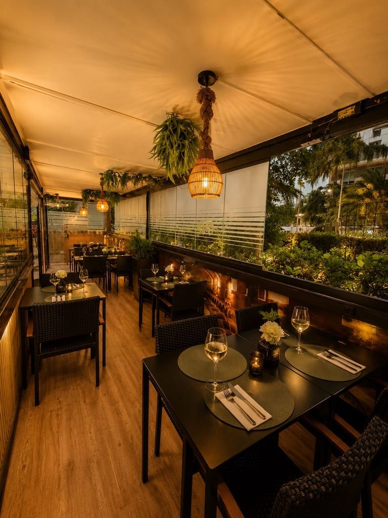 Terraza cubierta con mesas, plantas y lámparas de mimbre